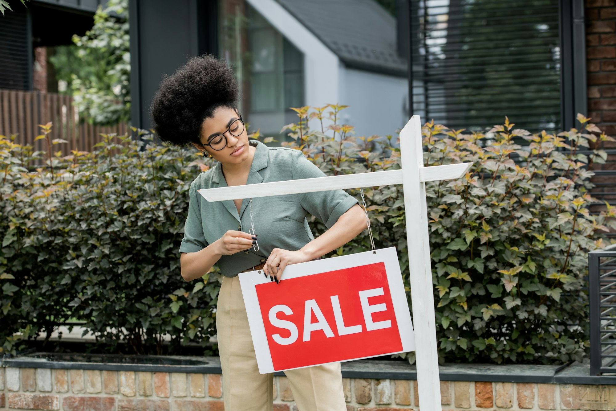 african american property agent hanging for sale signboard near house on city street