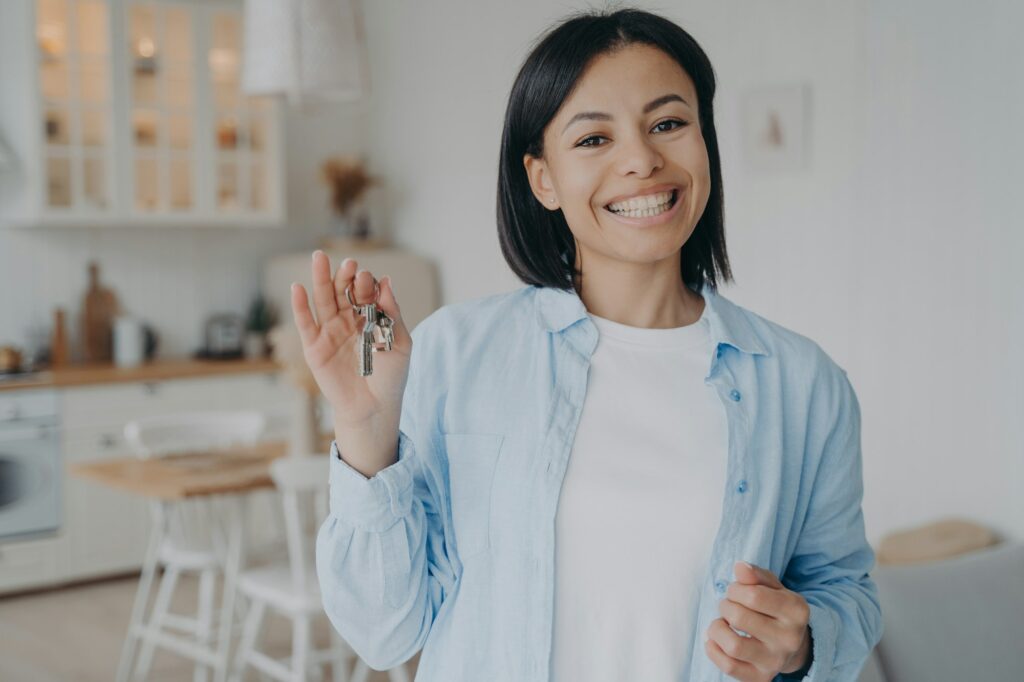 Smiling woman showing holding keys to new house. Real estate sale, rental. Mortgage advertisement